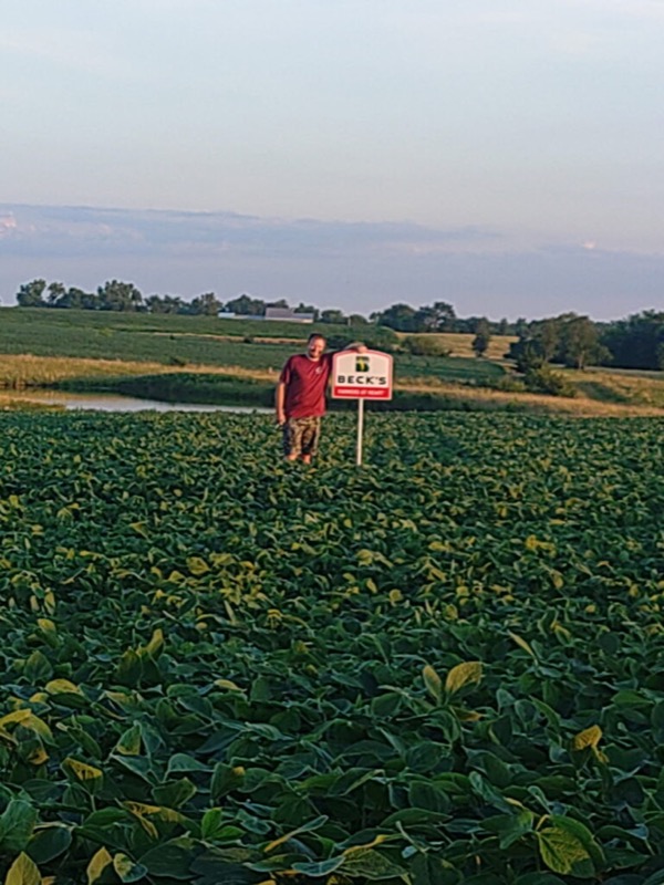A man standing beside a Beck’s sign in a soybean field