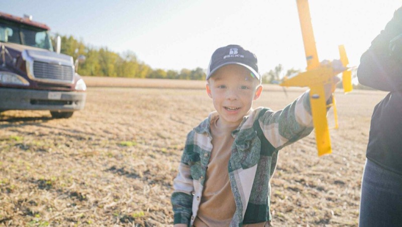 A young boy playing with a toy airplane in a harvested field