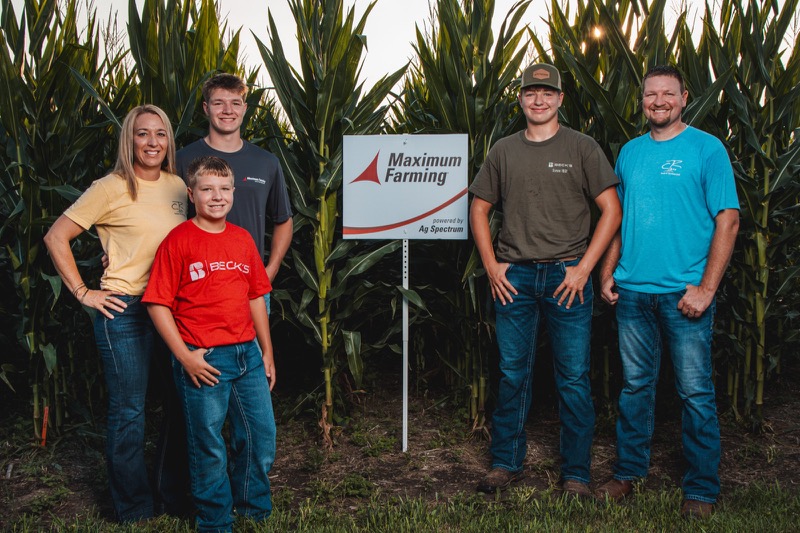 The Robinson family beside a Maximum Farming by Ag Spectrum sign in a cornfield