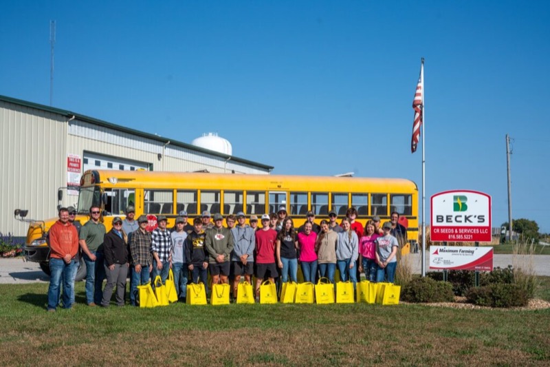 A group visiting the CR Seeds & Services warehouse with a school bus and Beck’s sign